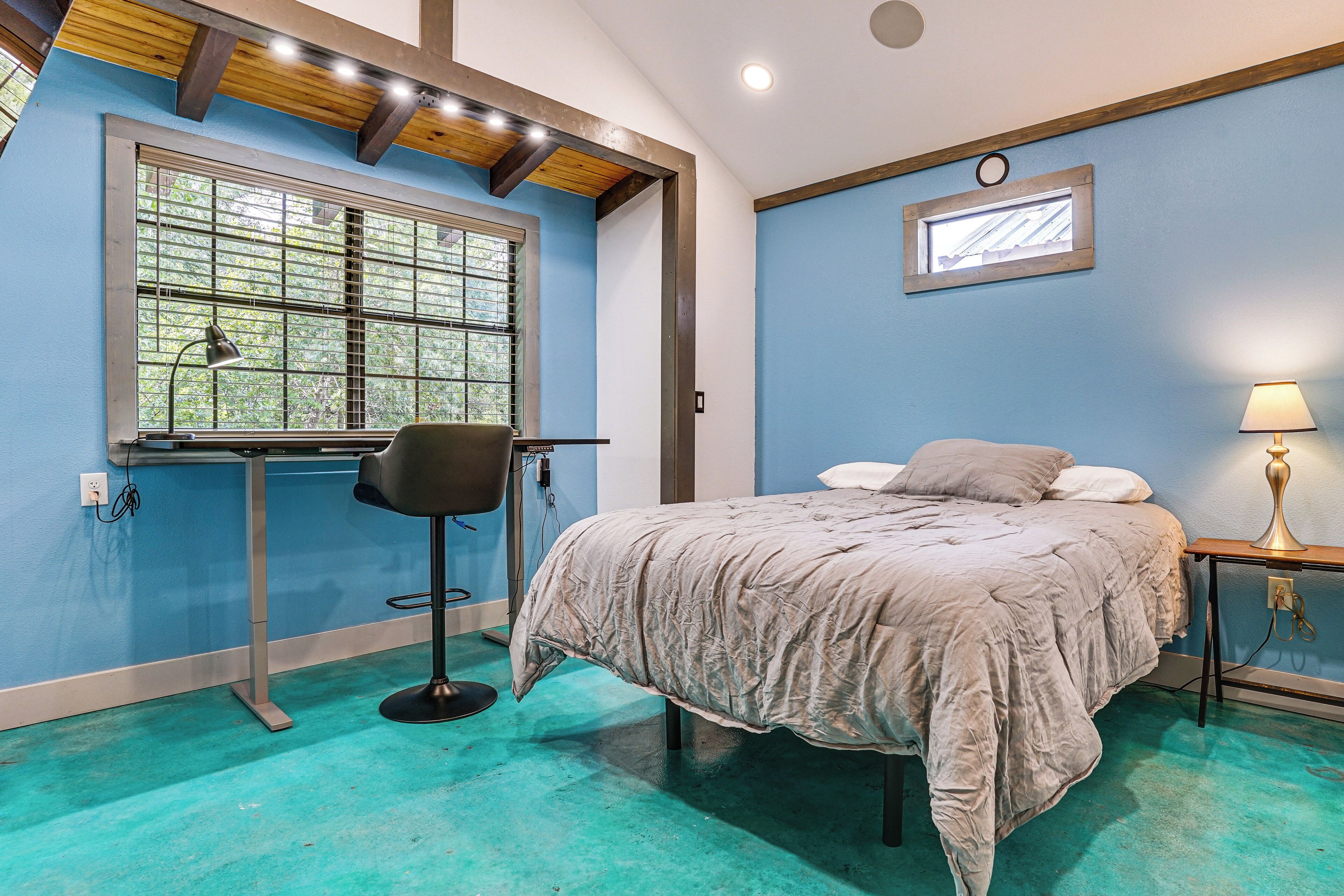 Quarto com cama, cadeira, escrivaninha, janela e um quadro na parede.