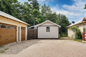 A residential property with a gravel driveway, wooden garage doors, and a small shed with a window.
