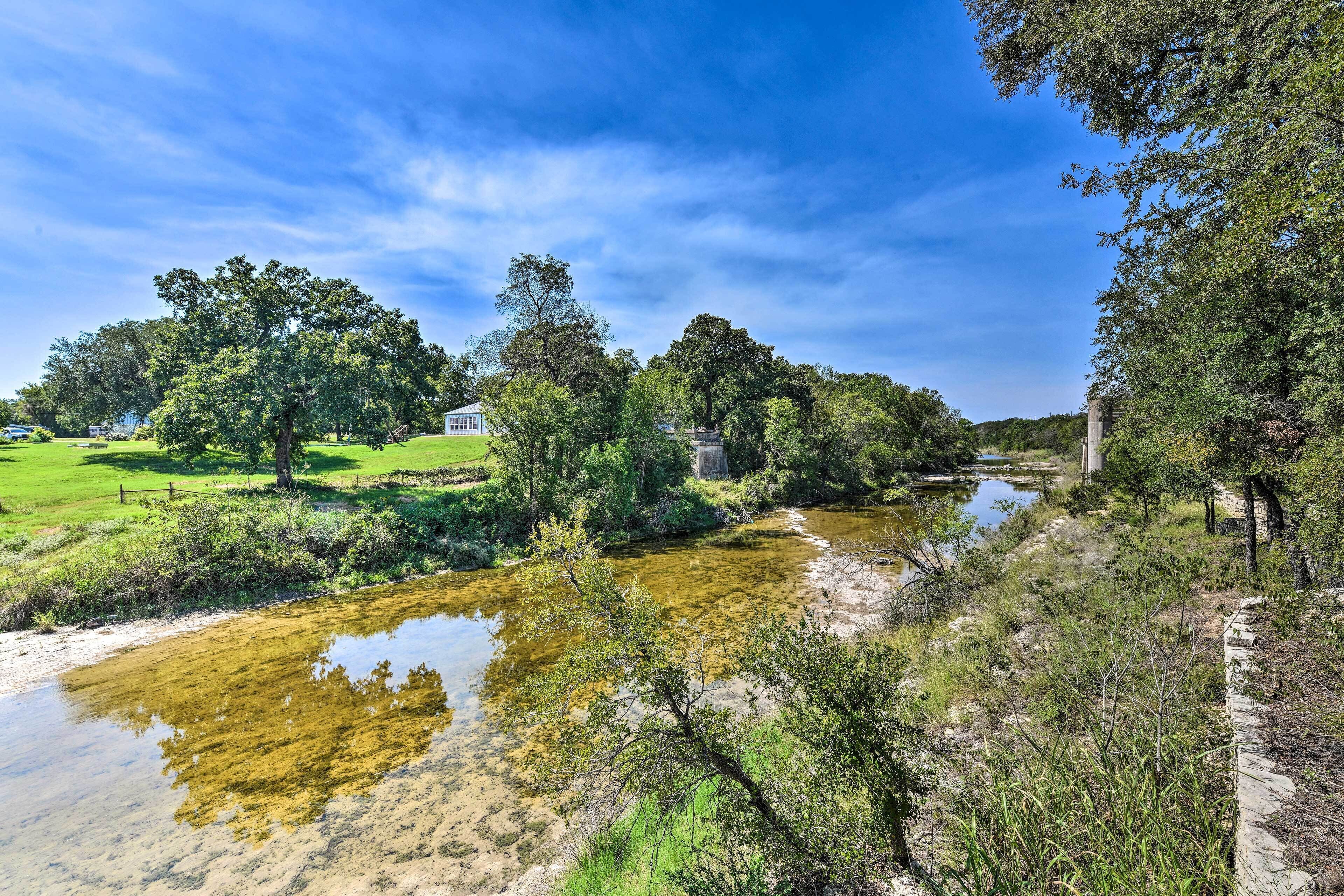 A river flowing through a park with trees and a small house in the background.