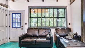 A room with a large window, a brown leather sofa, and a matching ottoman. - Paluxy Riverfront Couples Studio on Over 2 Acres! (Glen Rose)