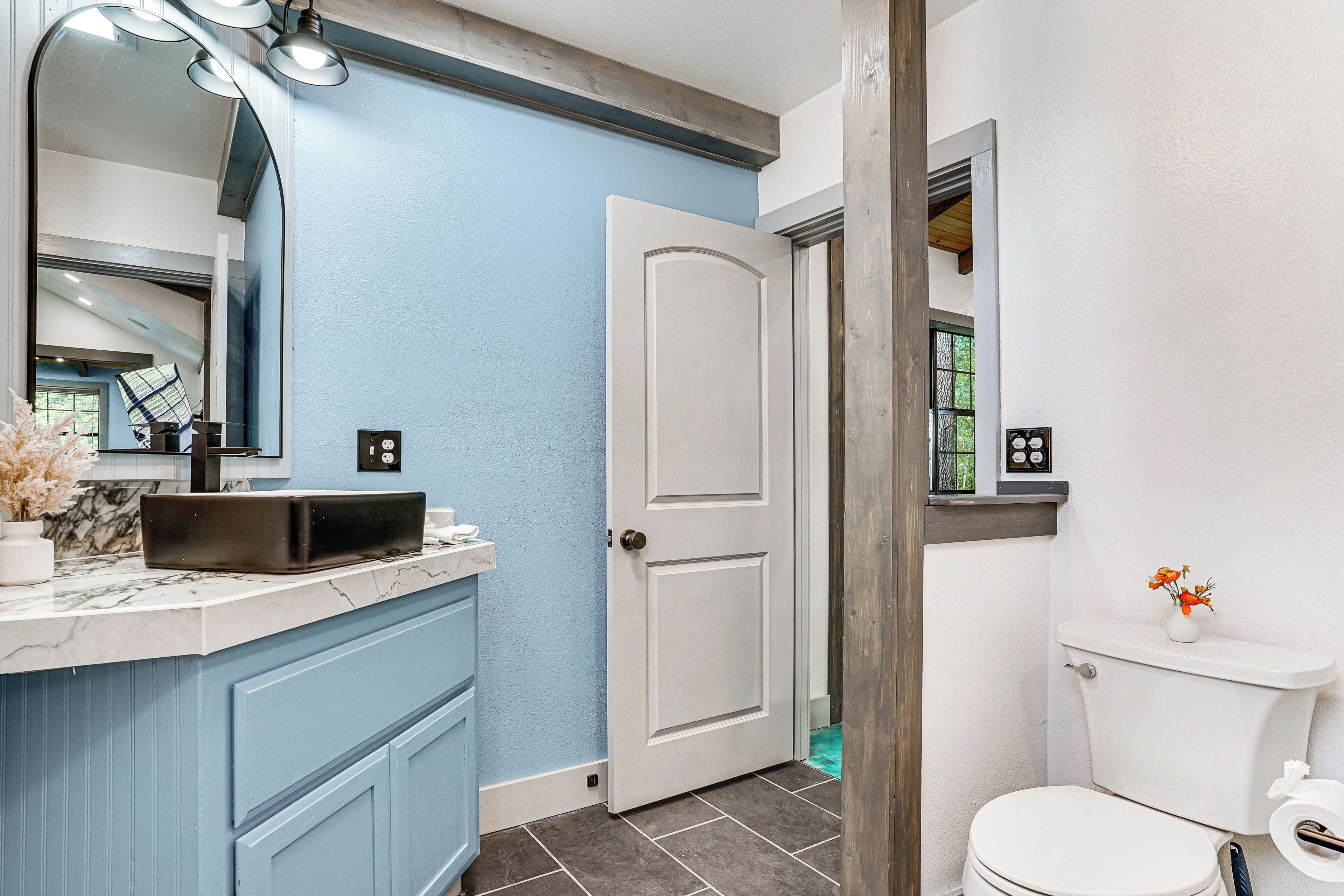 A bathroom with a marble countertop, a white door, and a toilet with a flower vase.