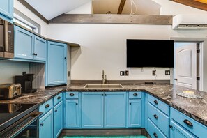 Eine Küche mit blauen Schränken, einer Marmorarbeitsplatte, einem eingebauten Ofen und einem Flachbildfernseher über der Spüle.