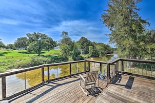 Terraza de madera con un banco que da a un río y un área verde con árboles.