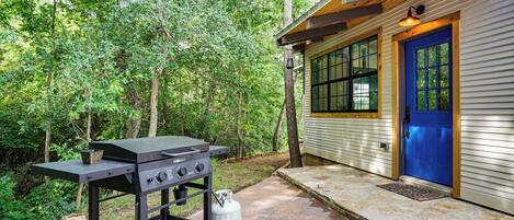 A grill outside a house with a blue door, surrounded by trees.