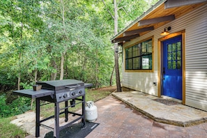 Una barbacoa davant d'una casa amb una porta blava, envoltada d'arbres.