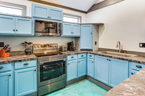 A kitchen with blue cabinets, stainless steel appliances, and a marble countertop.