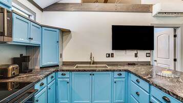 A kitchen with blue cabinets, a marble countertop, a built-in oven, and a flat-screen TV mounted above the sink.