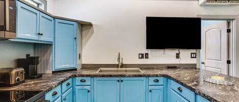 A kitchen with blue cabinets, a marble countertop, a built-in oven, and a flat-screen TV mounted above the sink.