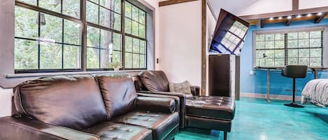 A room with a large window, a black leather sofa, a small table, and a chair.
