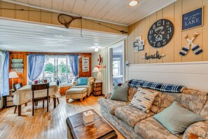 A cozy cabin interior with a dining area, a sofa, a clock, and a sign that says 'Welcome to the Lake.'