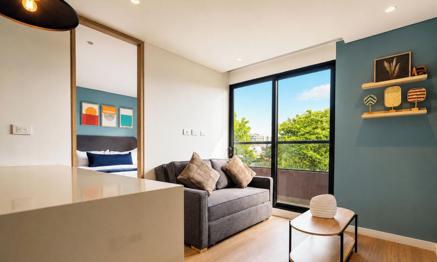 A modern living room with a sofa, a small table, and a large window offering a view of greenery.