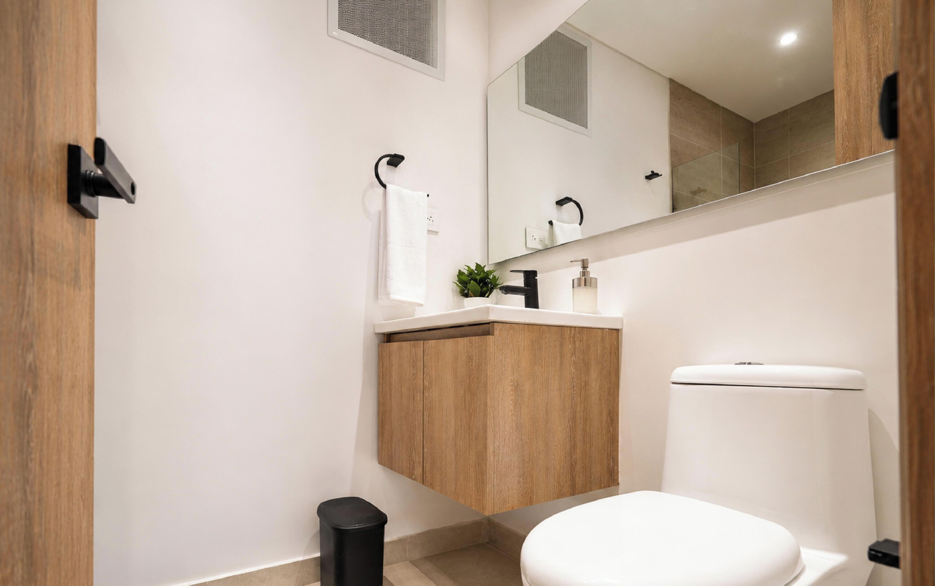 A modern bathroom with a wooden vanity, a white toilet, and a mirror above the sink.