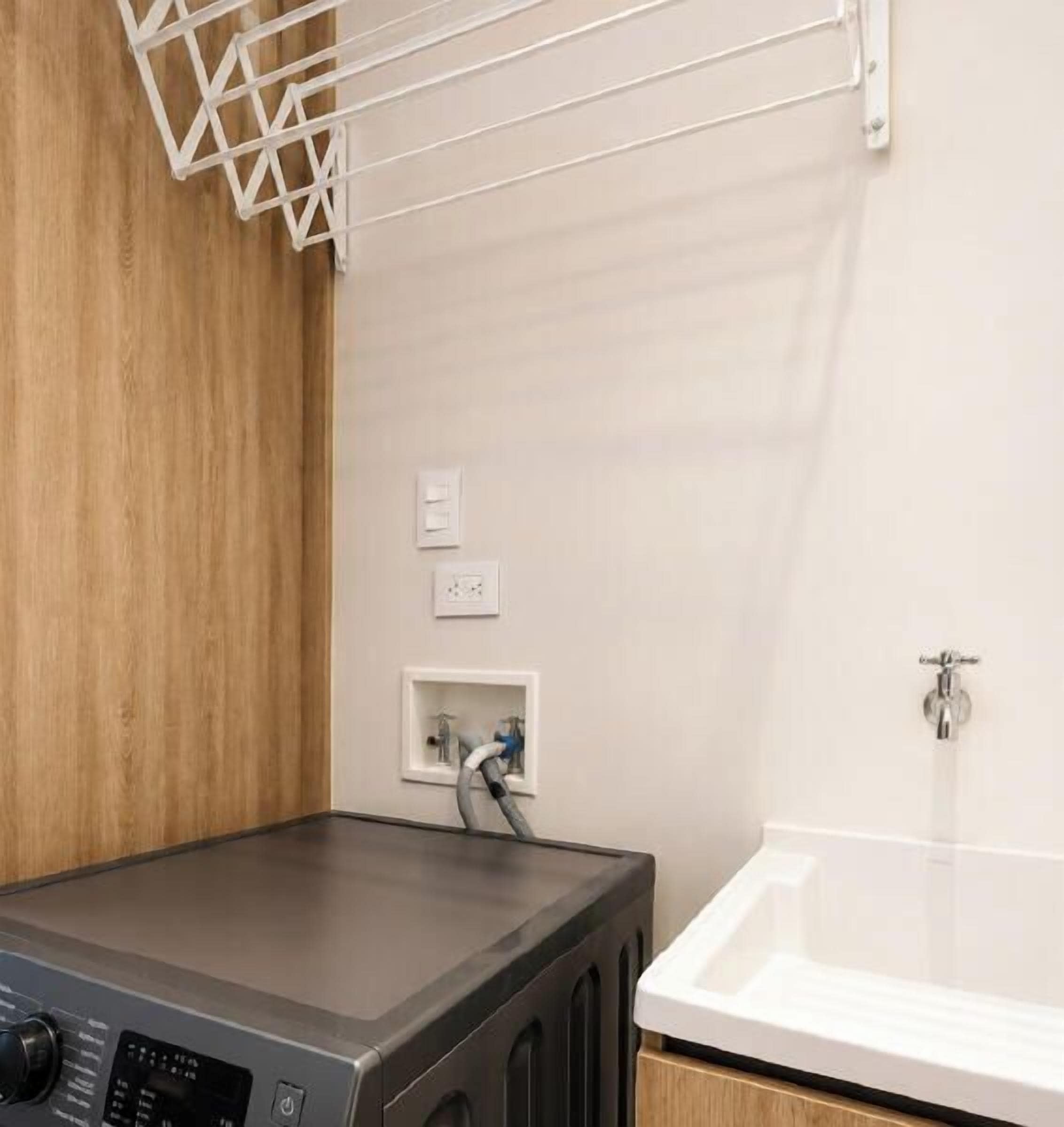 A laundry area with a washing machine, a drying rack, and a white bathtub.