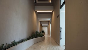 Un pasillo largo y estrecho, con una jardinera curva con follaje a un lado y una puerta al otro.