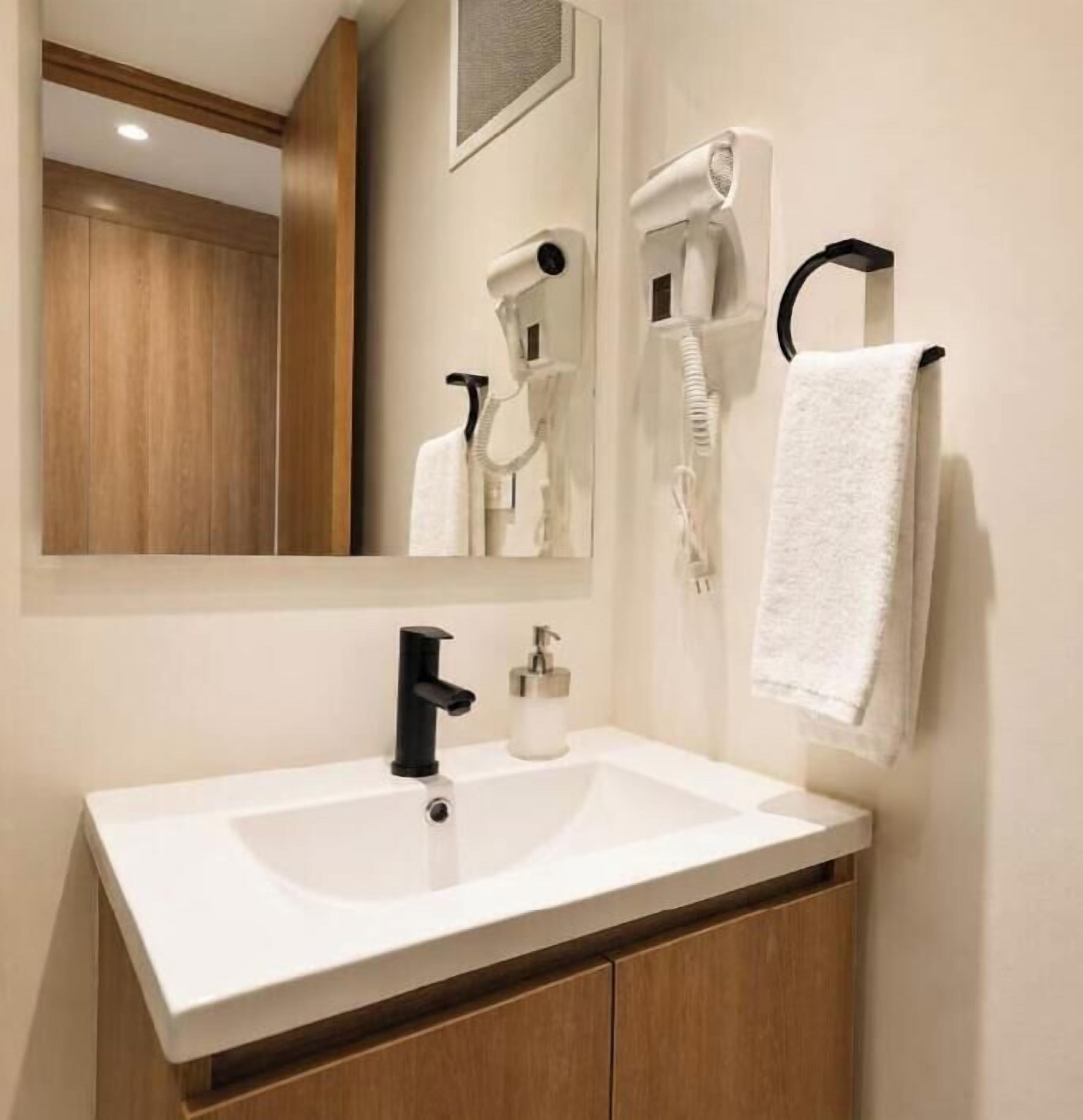 Ein Badezimmer mit einem weißen Waschbecken, einem Spiegel, einem Föhn und einem Handtuch, das an der Wand hängt.