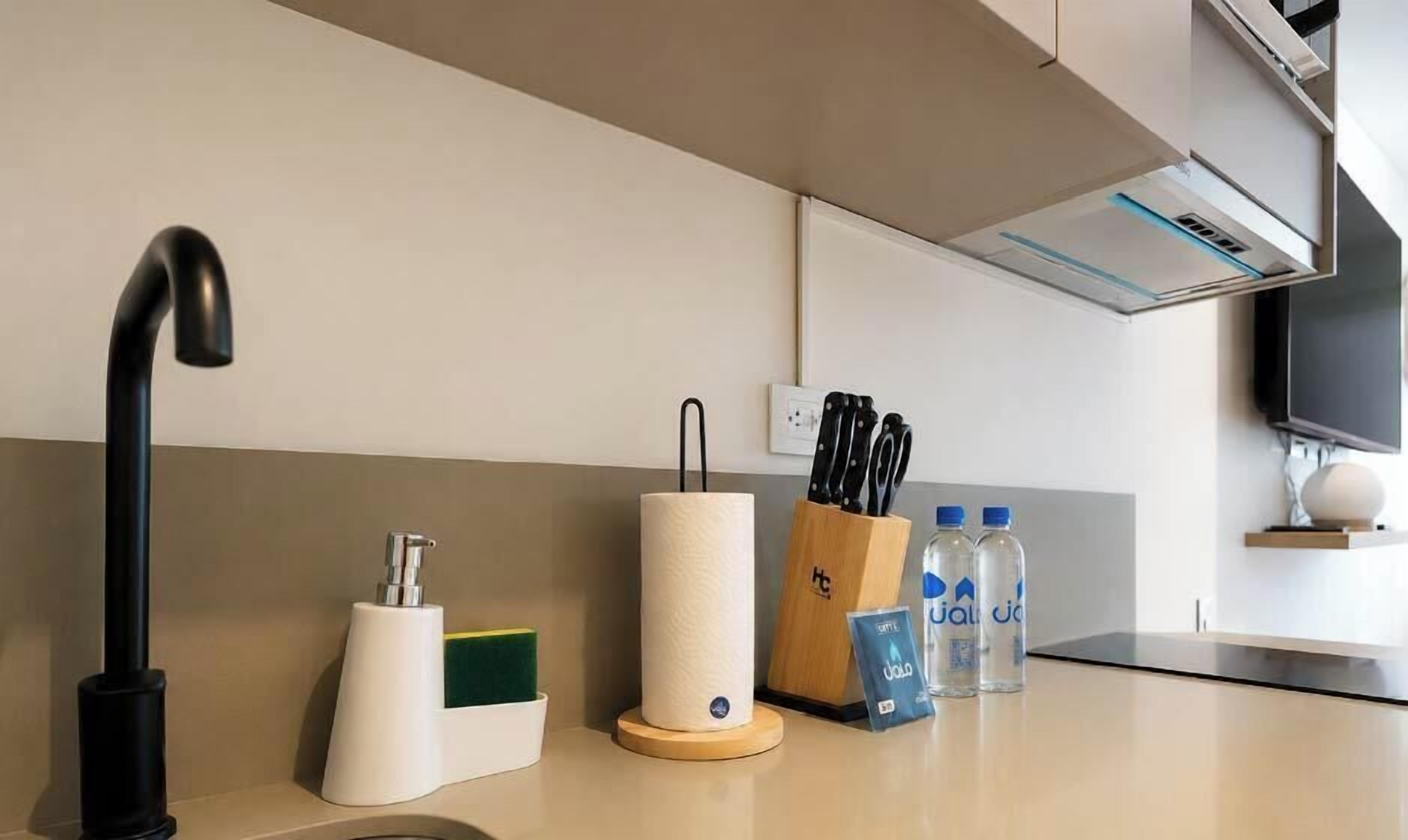 Una cocina moderna con un grifo negro, un dispensador de toallas de papel, un bloque de cuchillos y botellas de agua sobre la encimera.