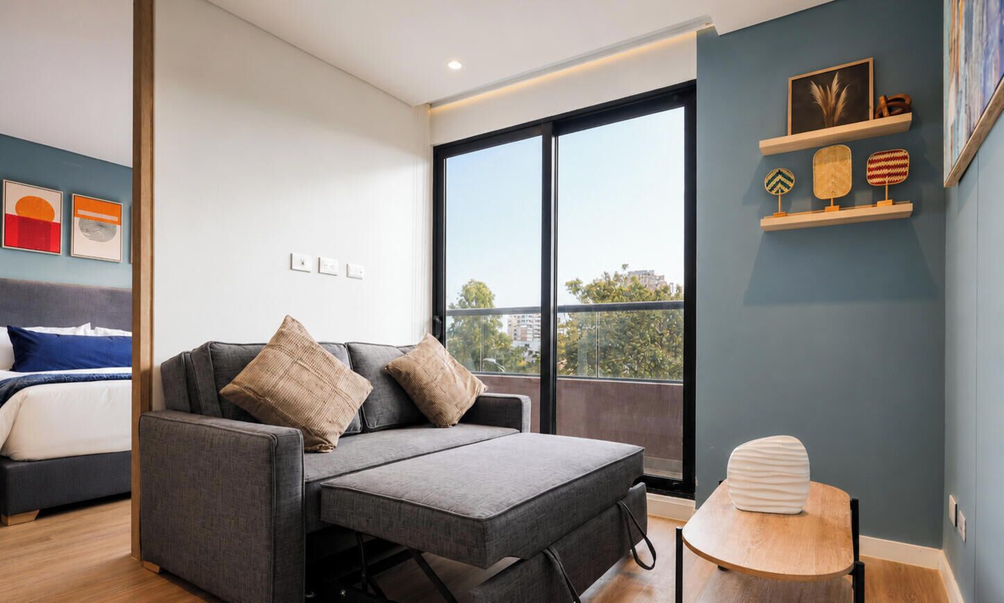 A modern room with a sofa, a small table, and a bed. There is a large window providing a view outside.