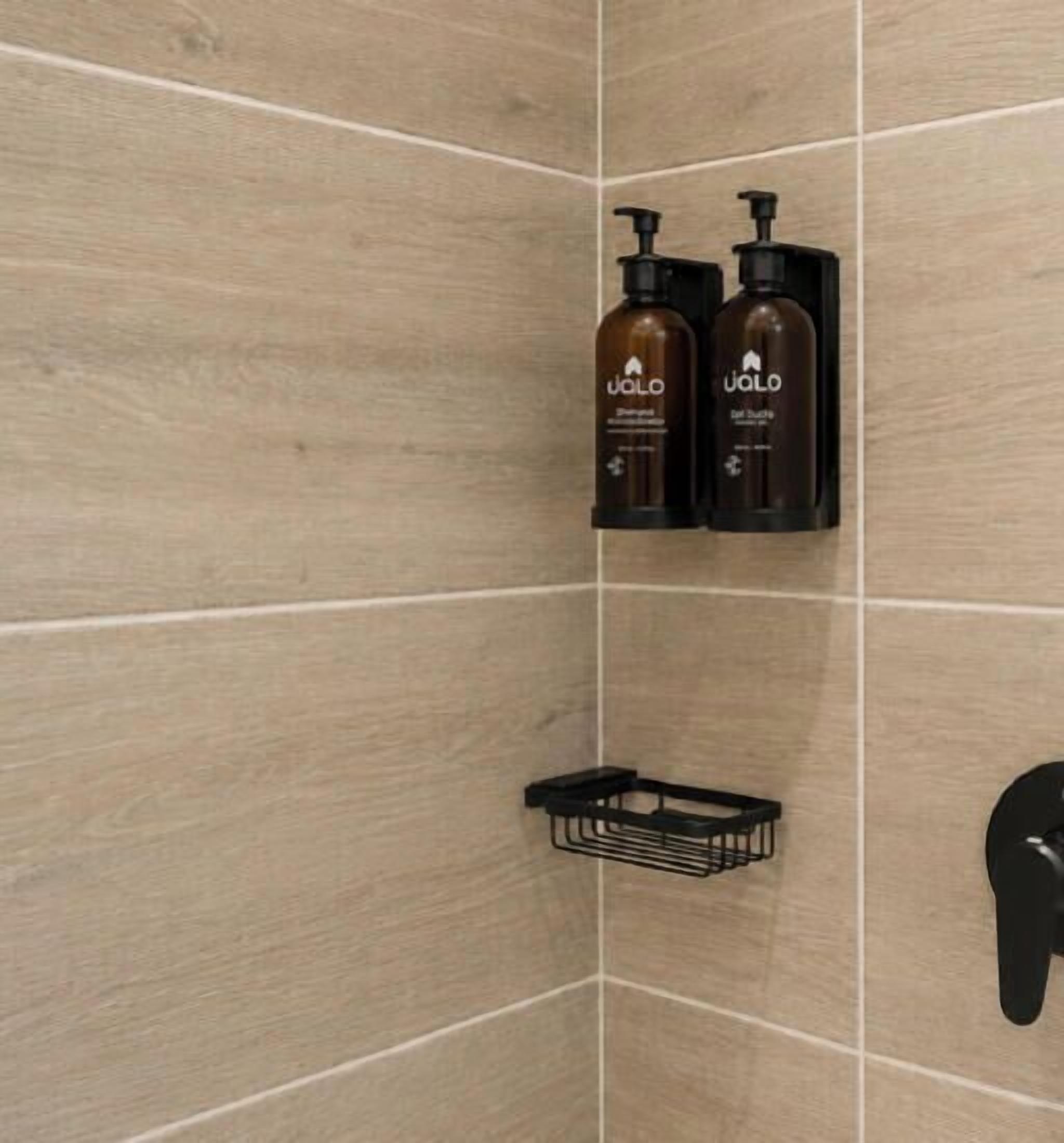 Et badeværelse med træfliser, to flasker UALO shampoo og en sort sæbeskål.