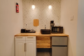 Eine kleine Küche mit Holzarbeitsplatte, einer Mikrowelle, einer Kaffeemaschine, einem Schneidebrett und einem Kühlschrank.