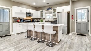 Una cocina moderna con armarios blancos, una isla central con taburetes de bar, electrodomésticos de acero inoxidable y una zona de café.