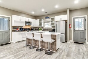 A modern kitchen with white cabinets, a central island with bar stools, stainless steel appliances, and a coffee bar. - Guyton Home w Pool, Theater & Arcade! (Guyton)
