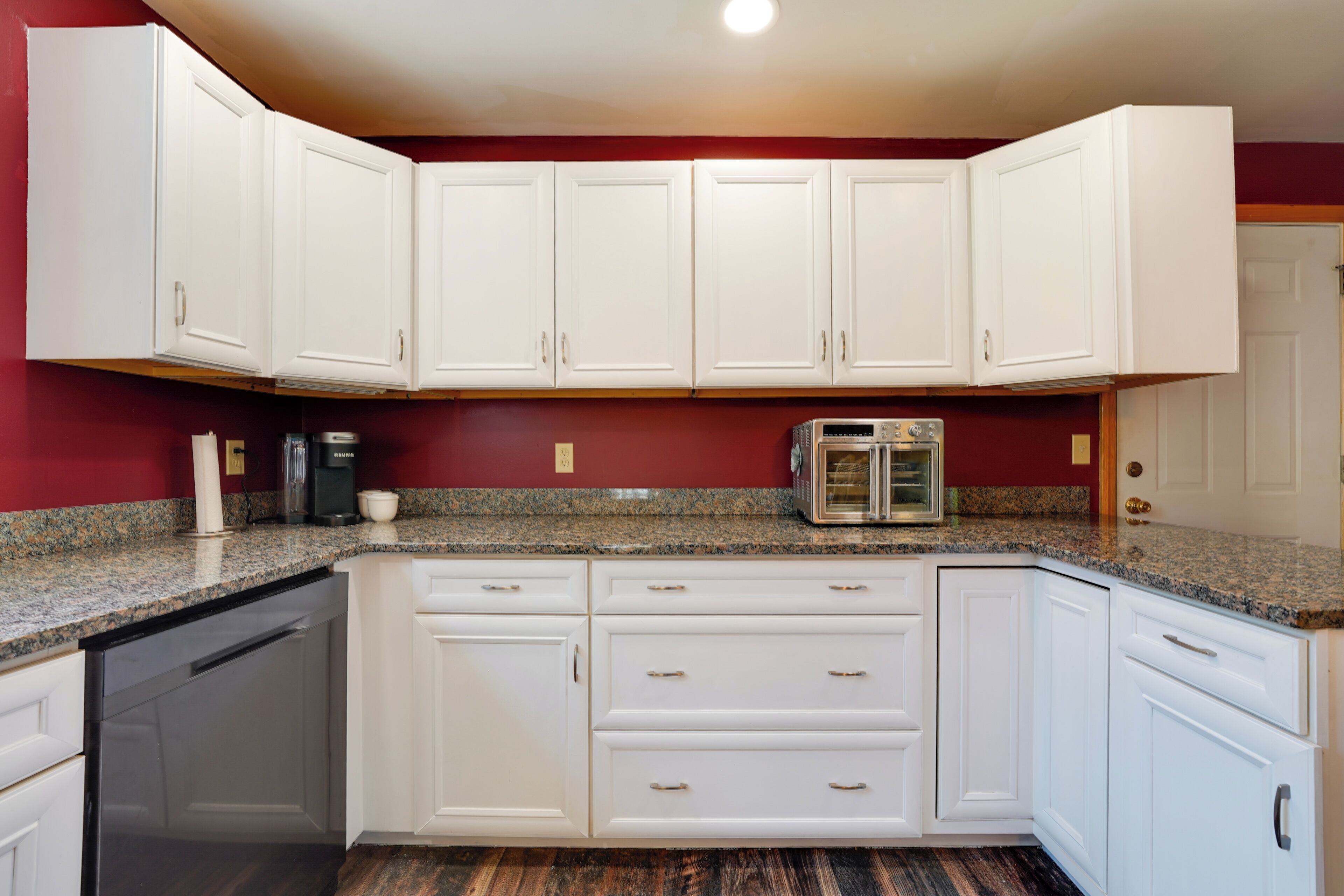 A kitchen with white cabinets, granite countertops, a coffee maker, and a built-in oven.