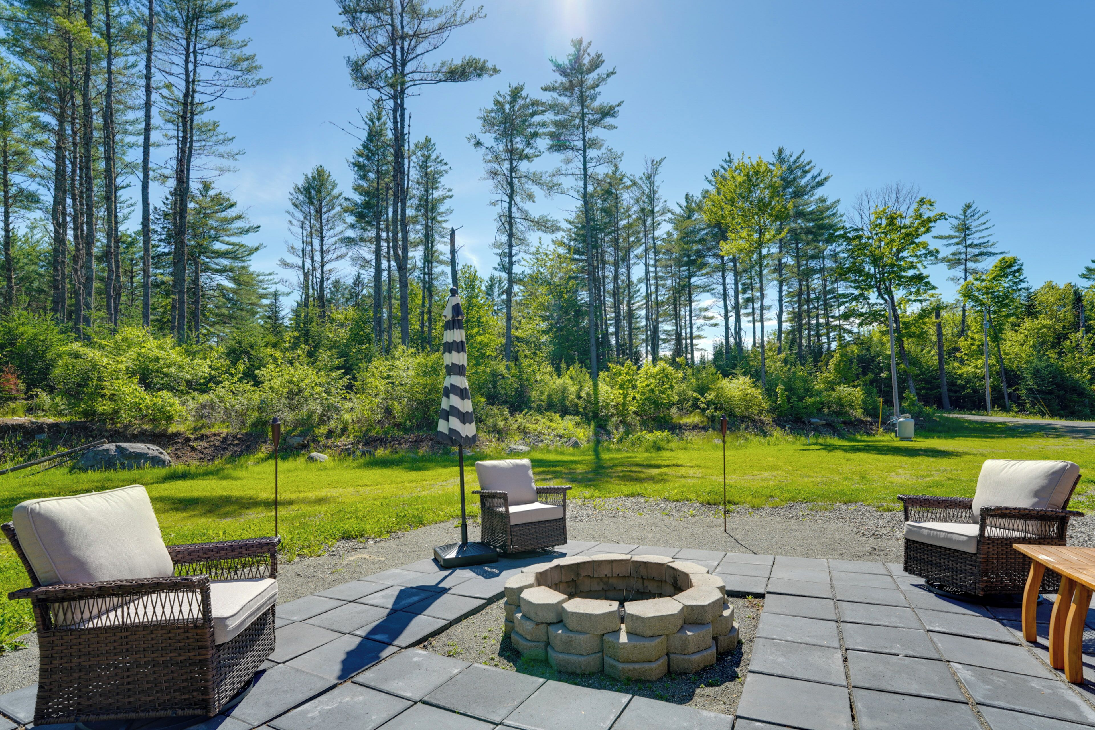 An outdoor seating area with wicker chairs, a fire pit, and a grassy lawn.