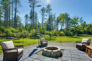 An outdoor seating area with wicker chairs, a fire pit, and a grassy lawn.