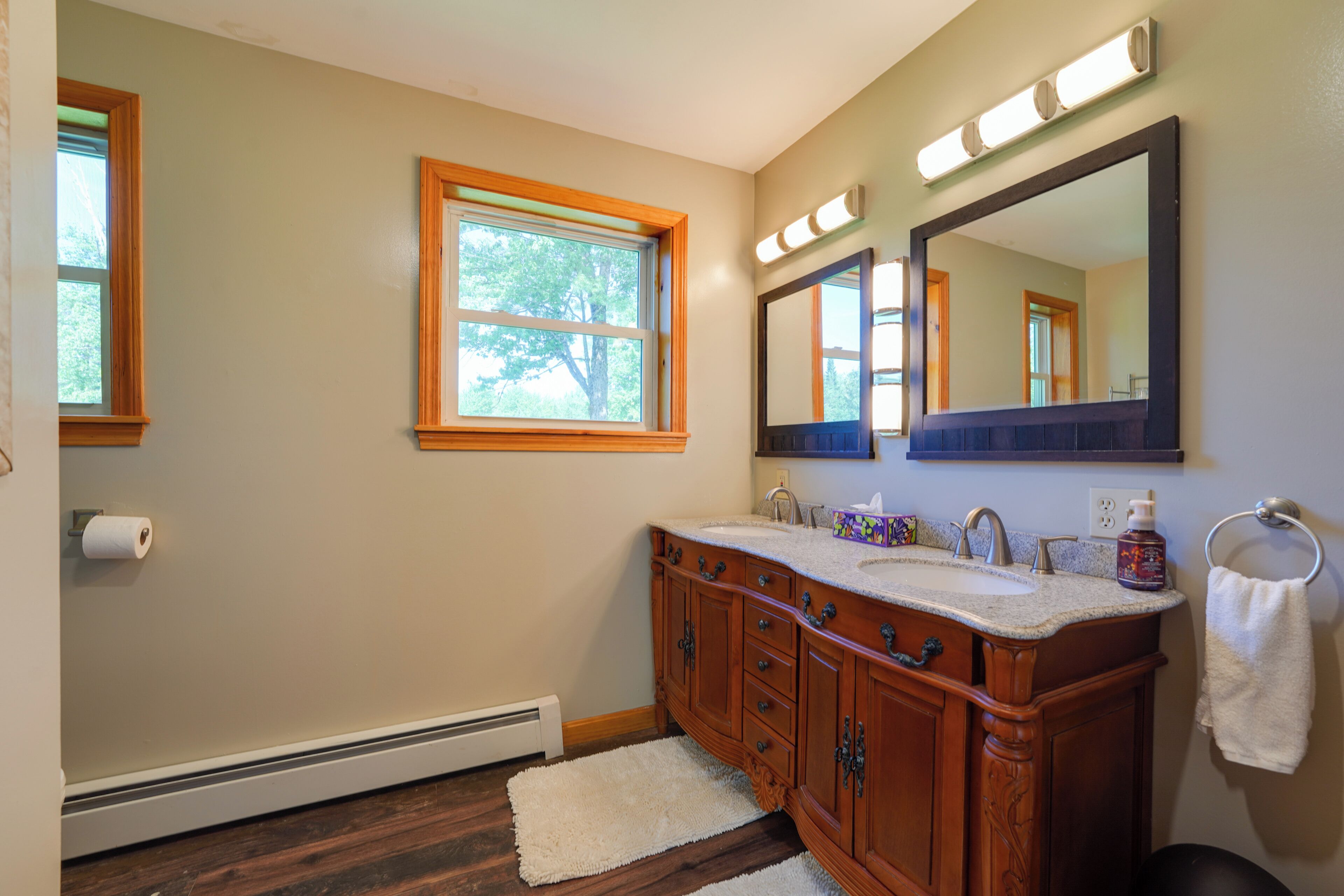 Une salle de bain avec des meubles en bois, un double vasque, un grand miroir et une fenêtre.