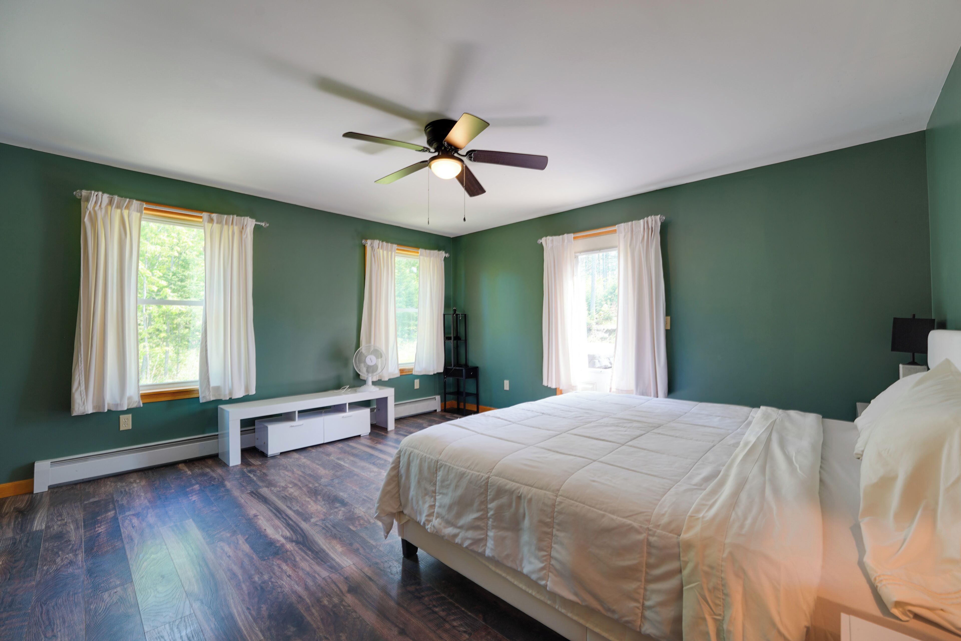 A bedroom with a bed, a ceiling fan, a bench, and two windows with curtains.