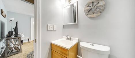 A bathroom with a white sink, wooden cabinet, and a toilet. There is a mirror with lights above it and a decorative wall piece.