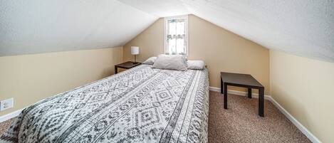 Un dormitorio con una colcha estampada, una mesita de noche y una ventana con cortinas.