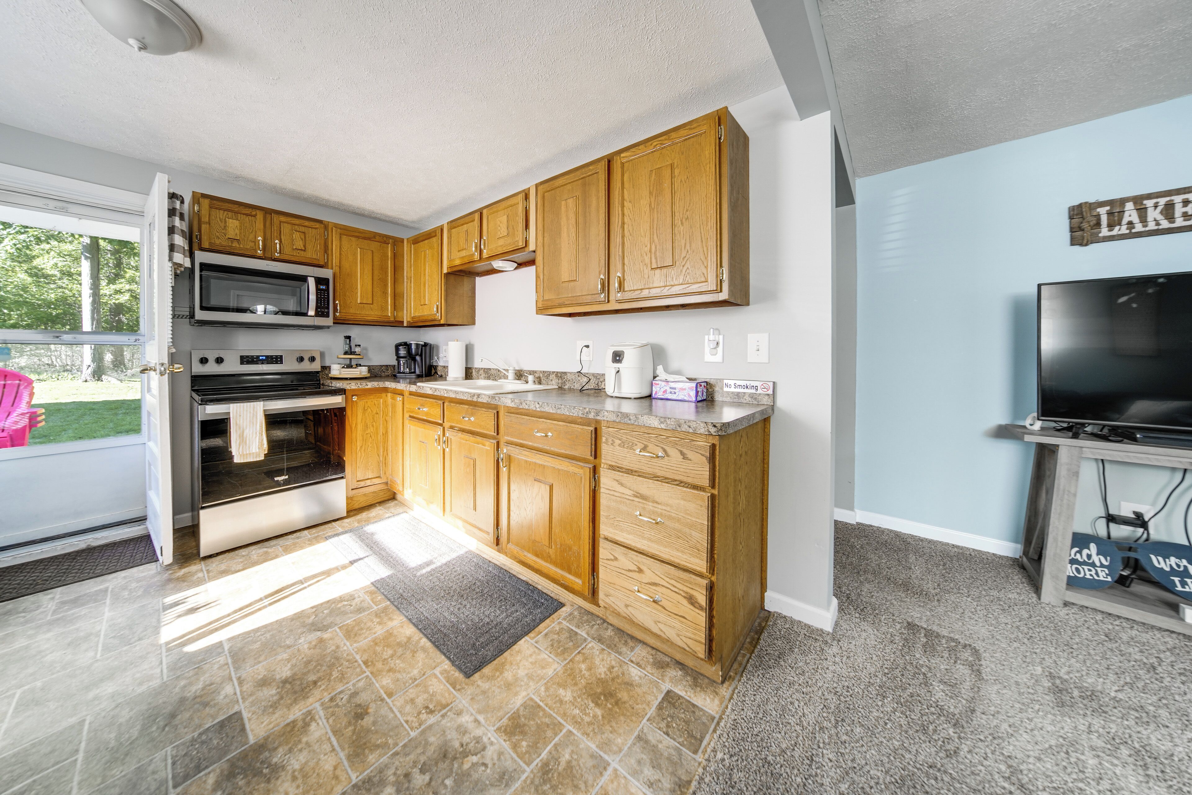 A kitchen with wooden cabinets, a microwave, oven, and a television.