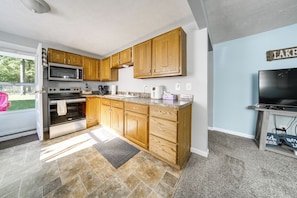 A kitchen with wooden cabinets, a microwave, oven, and a television. - Steps to Strip & Lake! Family-friendly Geneva Gem (Geneva)