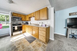Una cocina con armarios de madera, microondas, horno y televisor.