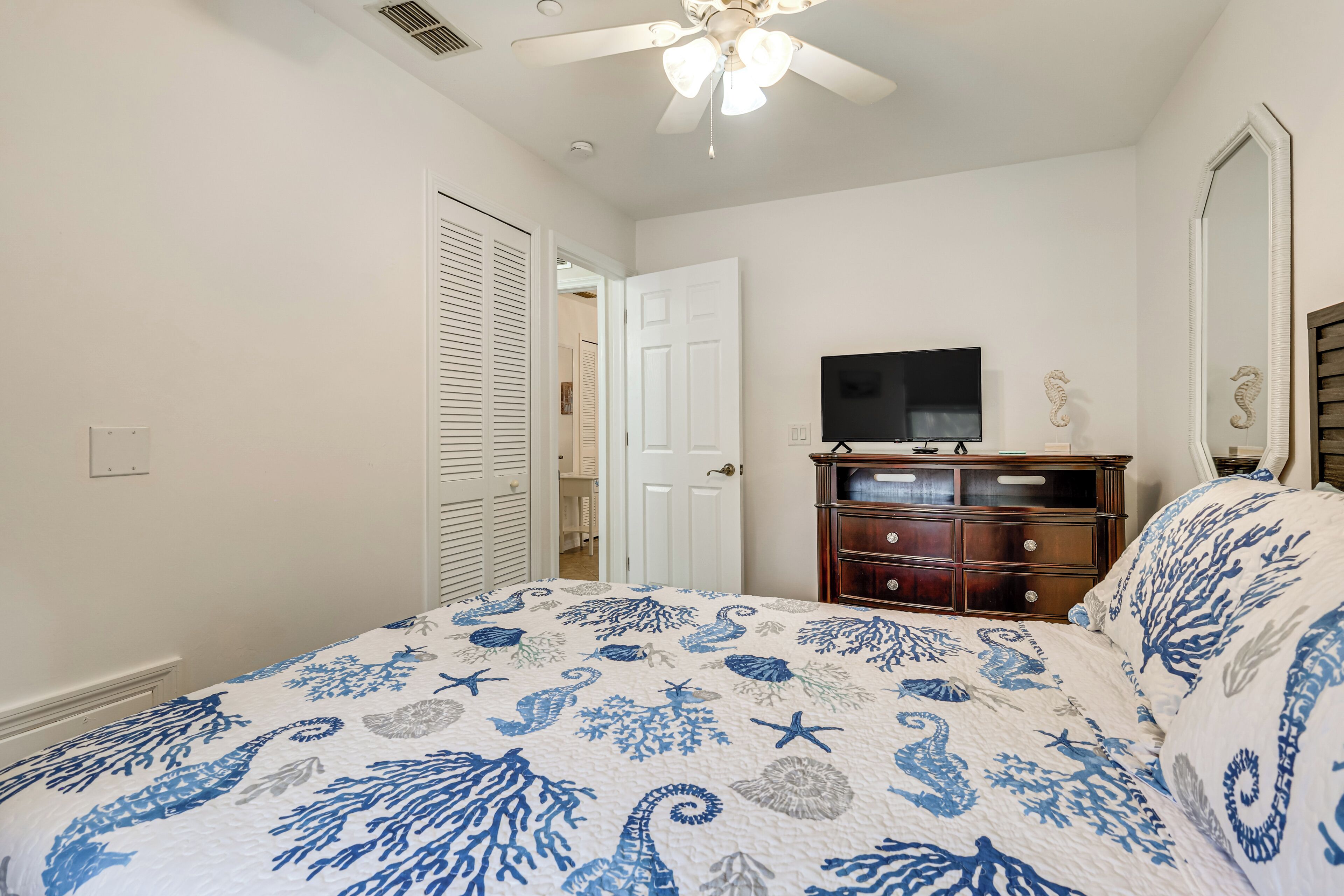 Quarto com cama, cômoda, televisão e ventilador de teto.