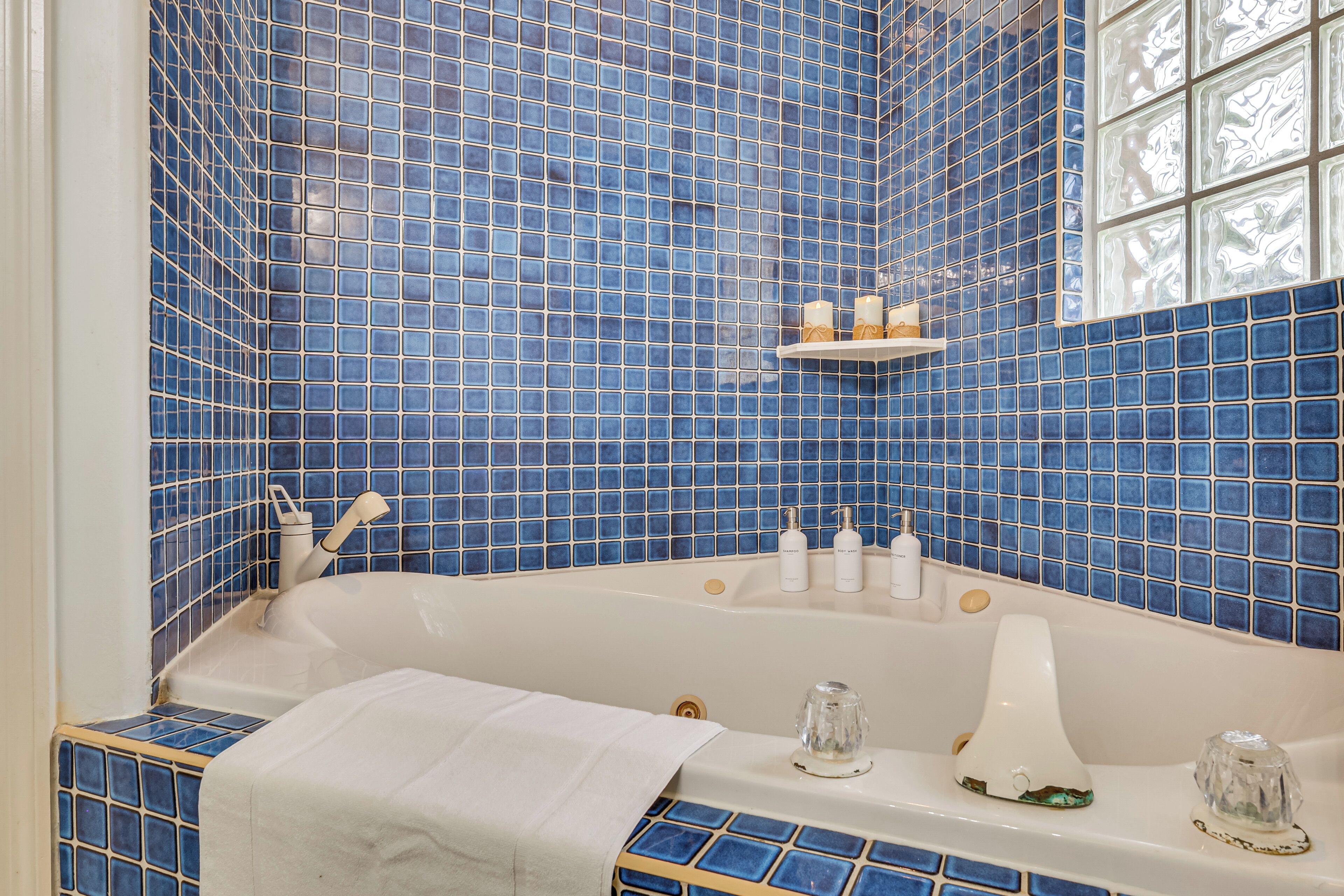 Een badkamer met een blauw betegelde muur, een witte badkuip en een plank met toiletartikelen.