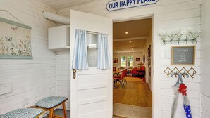 Una habitación con una puerta blanca, un banco, un cartel de bienvenida y un paraguas sujeto a la pared.