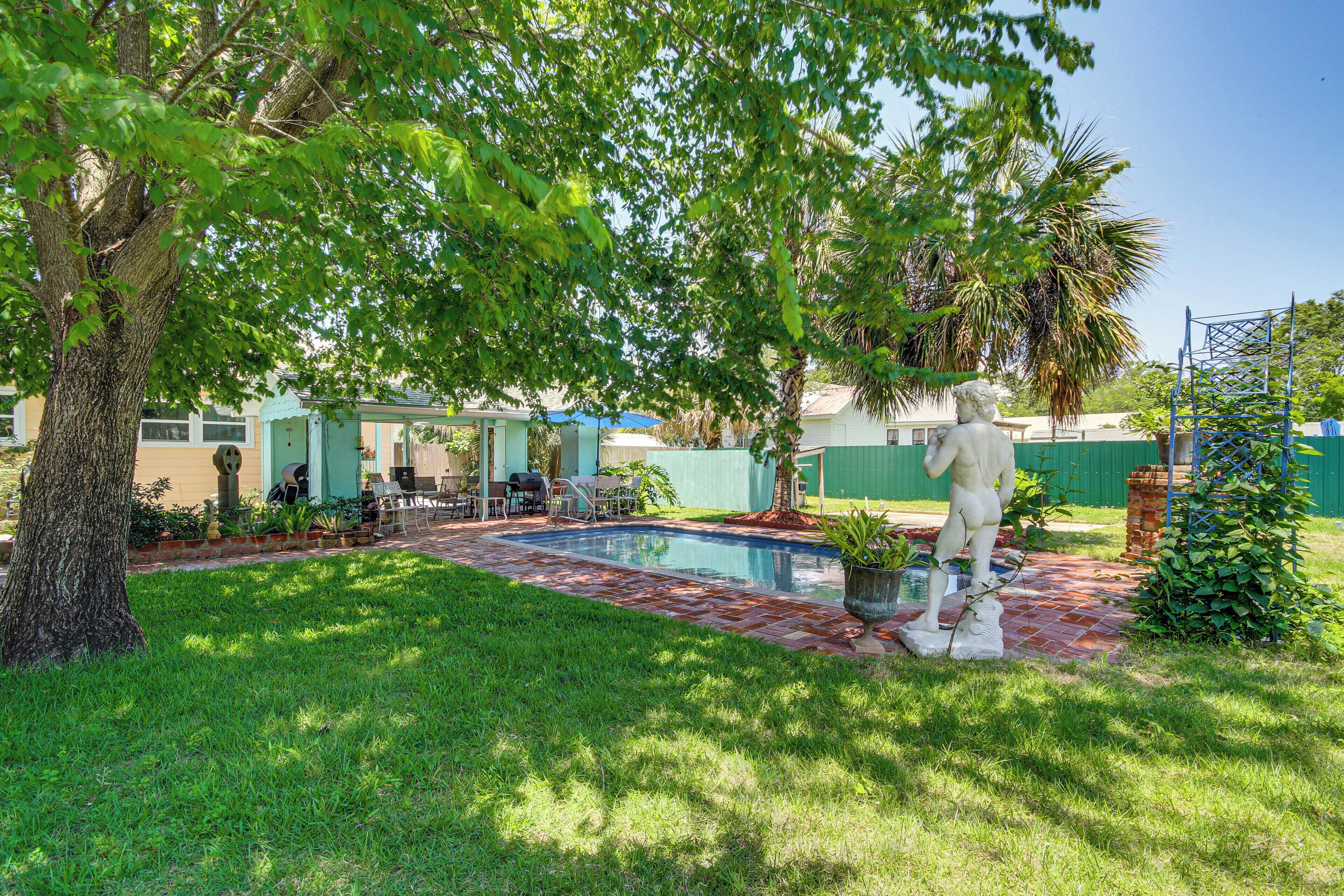 A backyard with a swimming pool, a statue, and a covered patio area.