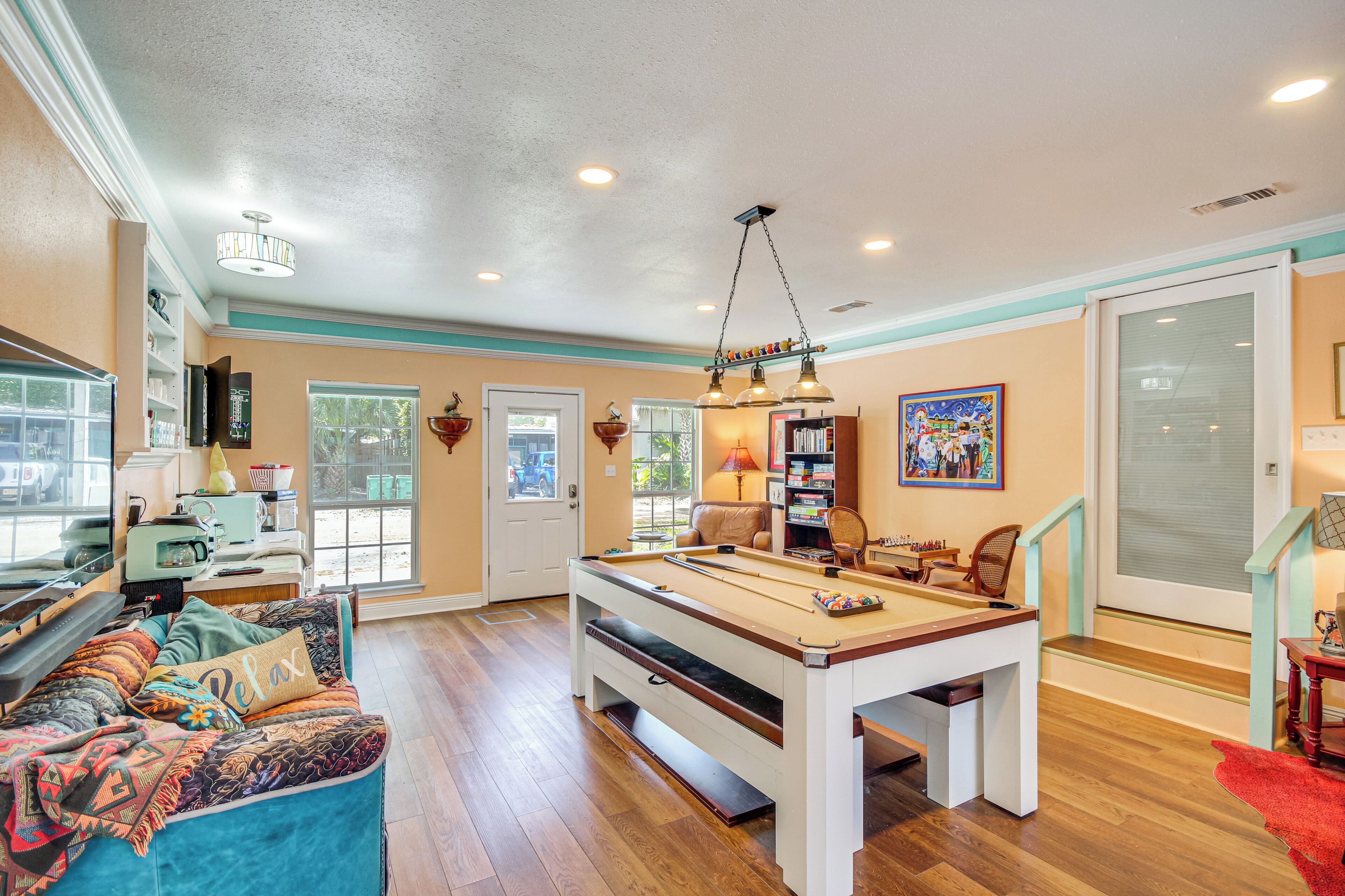 A pool table in a room with a sofa, a chair, a bookshelf, and a door leading to a balcony.