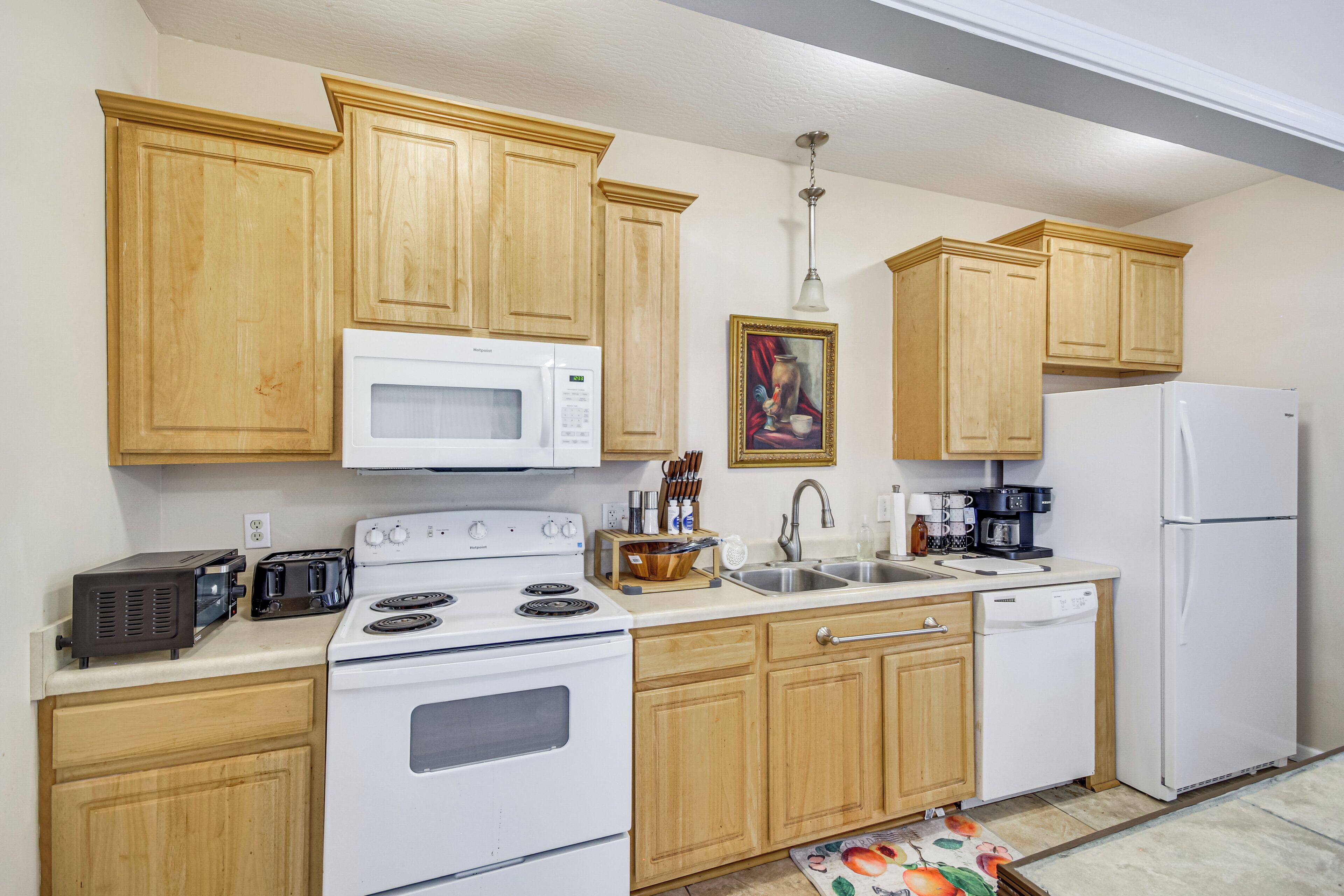 A kitchen with wooden cabinets, a white stove, a microwave, a refrigerator, and a coffee maker.