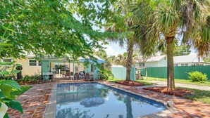 Una piscina con un patio de ladrillo, rodeada de vegetación y un pequeño espacio con muebles de exterior.