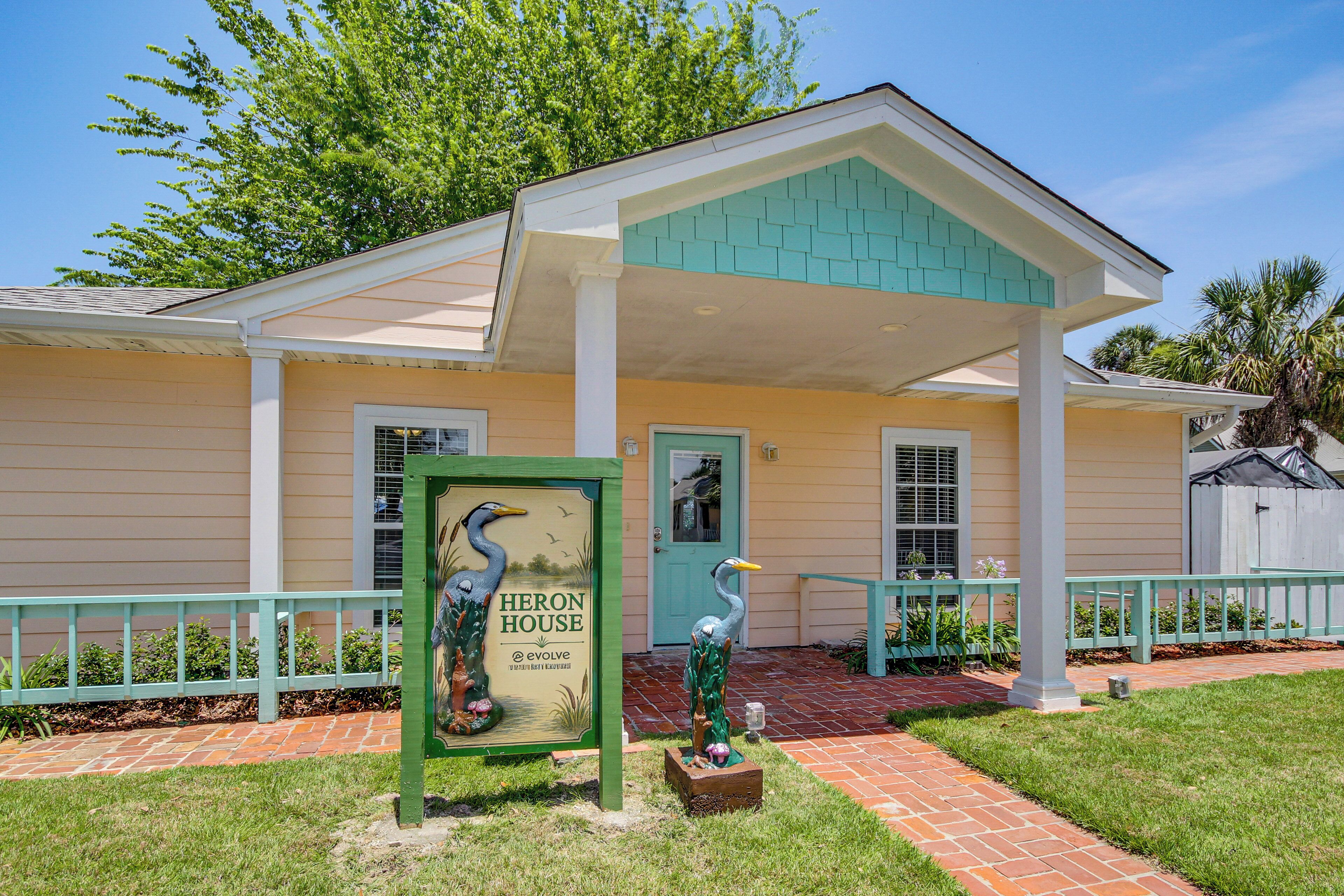 A house with a porch, a sign, and two bird sculptures.