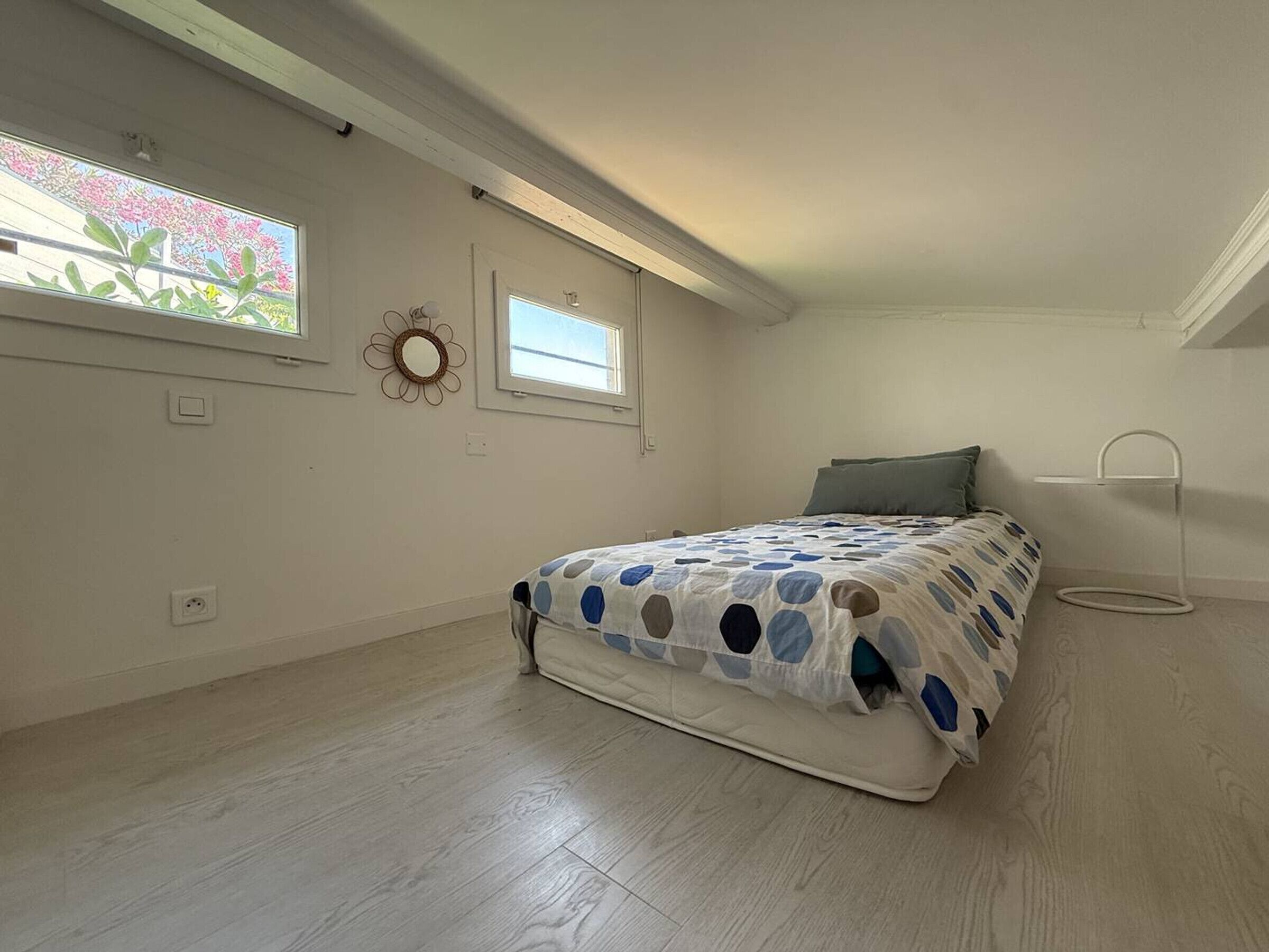 Un dormitorio con cama, ventana, espejo en la pared y una mesita.