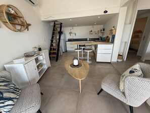 Ein modernes Wohnzimmer mit einer Couch, einem Couchtisch und einer Küchenzeile mit Theke und Barhocker.