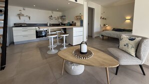 Una cocina moderna con muebles blancos, una isla central con taburetes y un comedor con una mesa redonda y un sofá estampado.