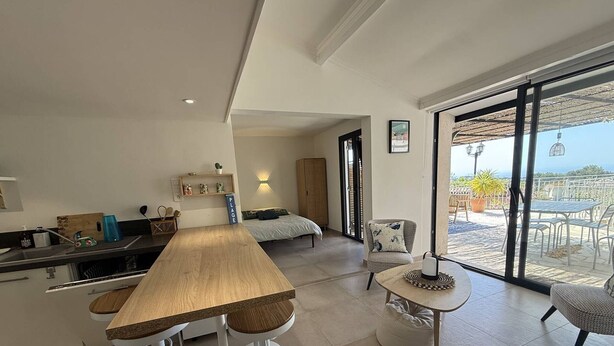 Una cocina moderna con una mesa de madera y taburetes, un comedor con una mesa redonda y sillas, y un balcón con mobiliario exterior.