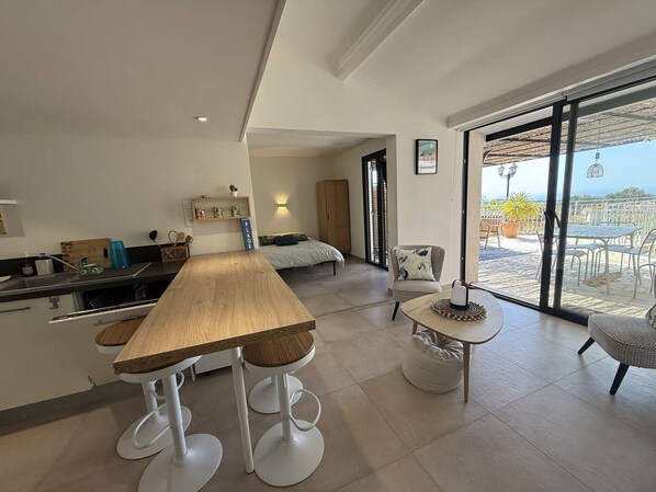 Eine moderne Küche mit Holztisch und Barhocker, ein Essbereich mit rundem Tisch und Stühlen sowie ein Balkon mit Sitzgelegenheit.