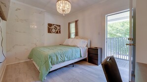 Et soveværelse med seng, stol, natbord, lysekrone, et vindue med skodder og en dør til balkon.