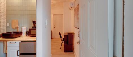 A narrow hallway with a kitchen area on one side, a door with a lock, and a wall-mounted light fixture.
